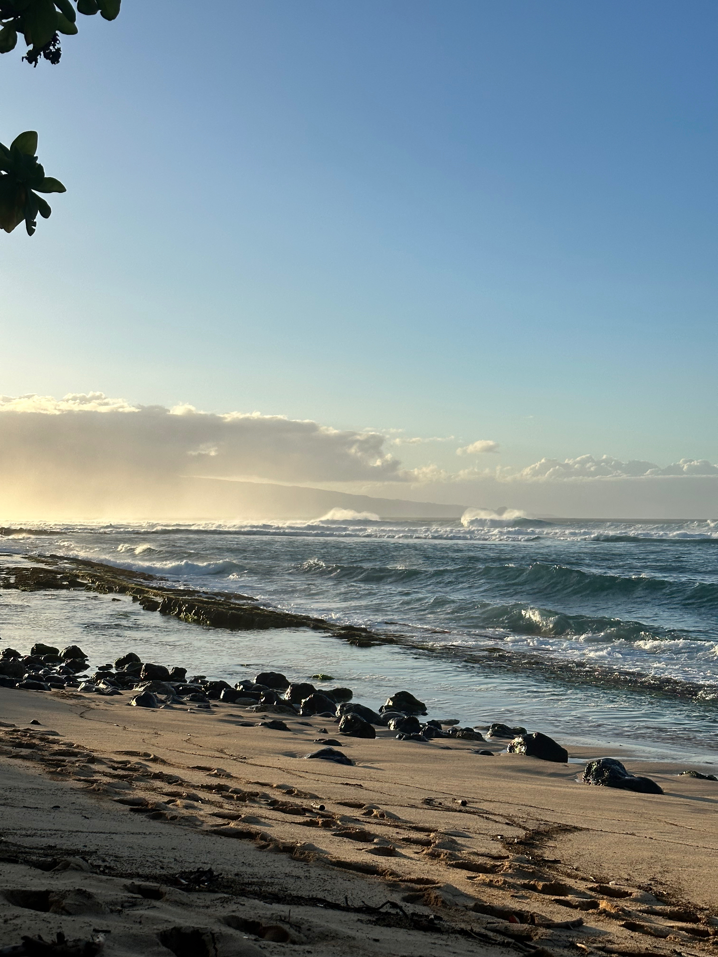 Morning waves rolling onto a quiet Maui beach with lava rock