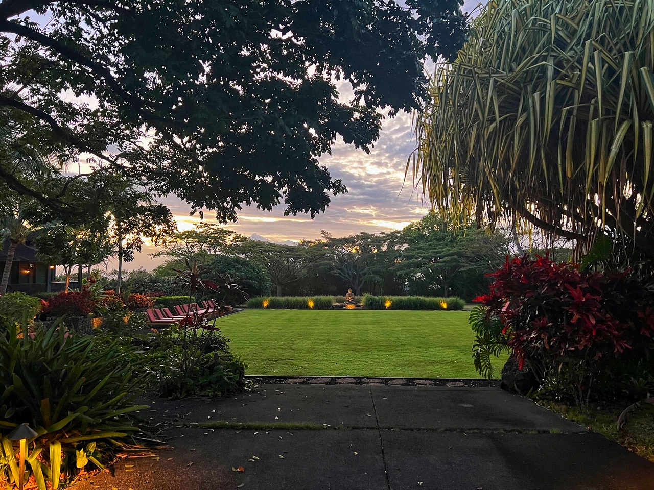 Sunset over a tropical Maui garden with a distant stone Buddha and quiet lounge chairs