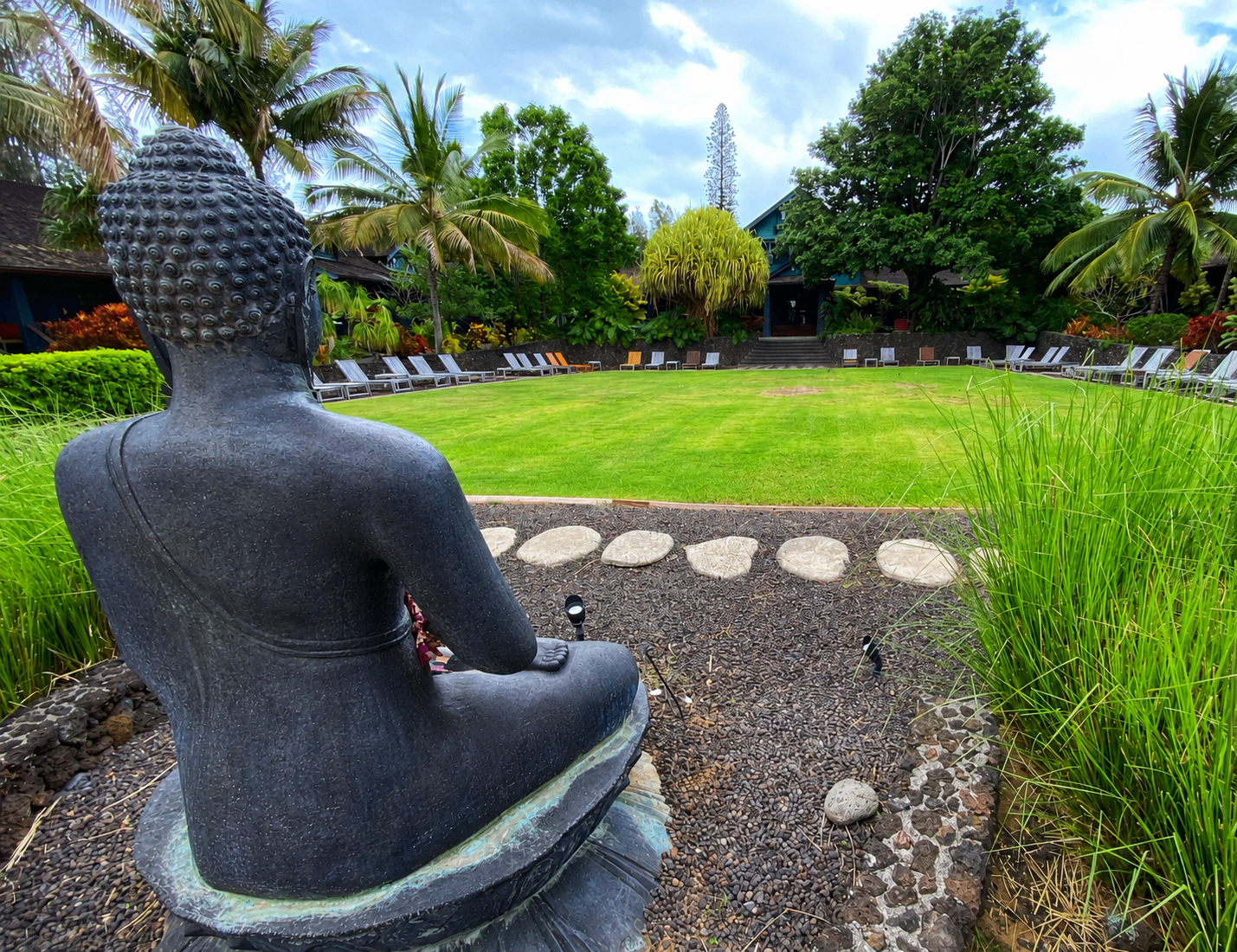 Bronze Buddha statue overlooking a tropical Maui garden and plantation cottage